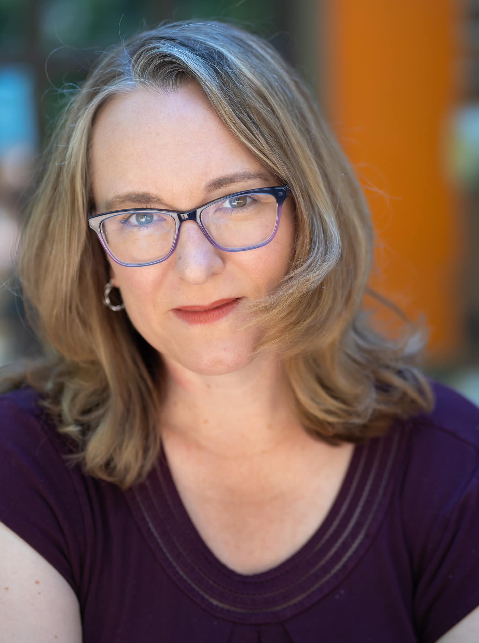 Portrait of Valerie Rachelle, Artistic Director and Dean of the Pacific Conservatory Theatre (PCPA). She is shown from the shoulders up, wearing glasses and a dark purple top, with shoulder-length light brown hair and a neutral background softly blurred behind her.